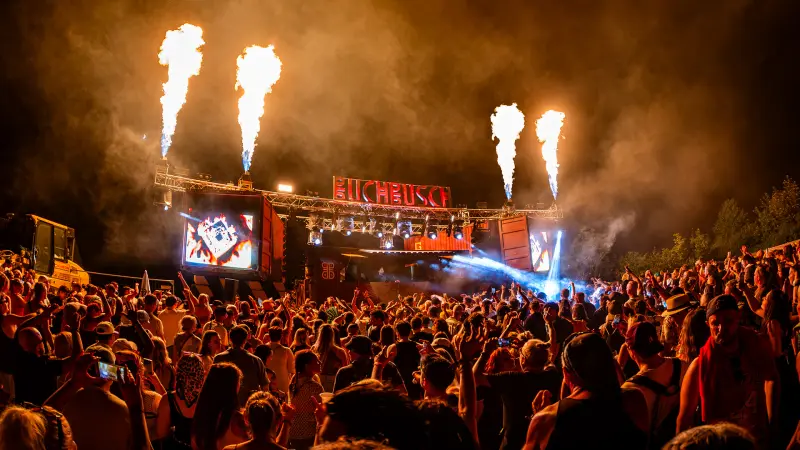Columns of flame above the Buchbusch Stage at night, the crowd in front in the stage lights